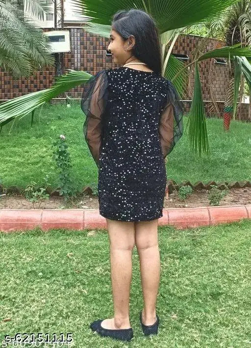 A woman in a black sleeveless dress with a sheer overlay, standing outdoors