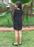 A woman in a black sleeveless dress with a sheer overlay, standing outdoors