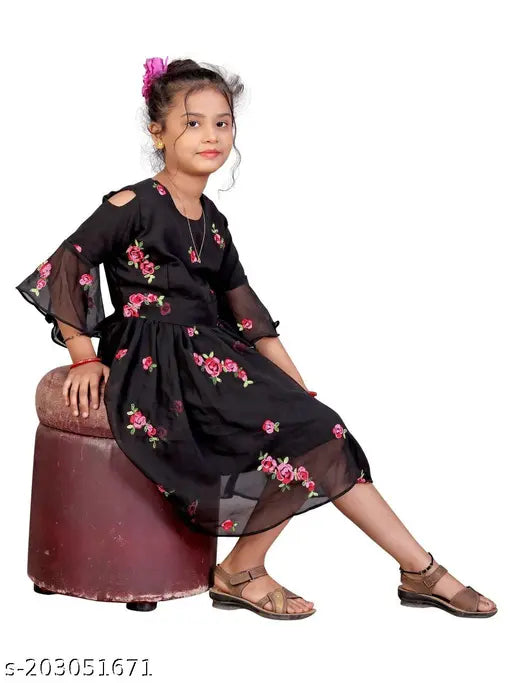 A young girl posing in a black, georgette embroidered dress with flared sleeves and skirt. The dress is of fitted style