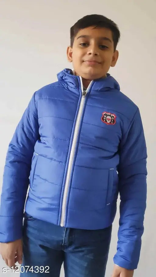 Boy in blue jacket with black trim and hood, standing against white wall