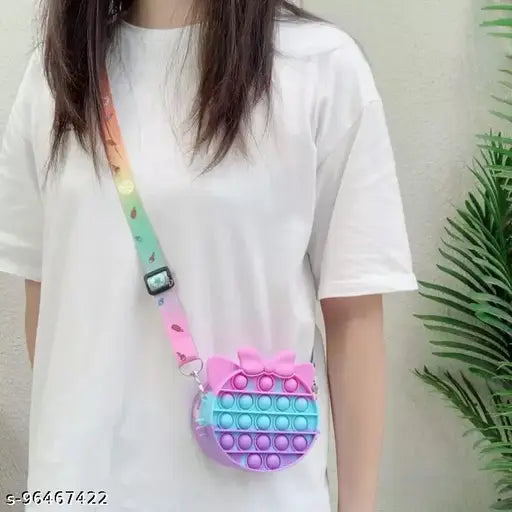 The image displays a brightly colored, playful sling bag with a pop-it feature and a pink bubble design. It has a silicone texture, resembling a fidget toy, which is often used for stress relief. The bag appears to be designed for children, given its youthful appearance and vibrant color scheme. It features multiple pouches and seems to have a coin purse function. The bag is designed with a shoulder strap for easy carrying and has a sturdy closure mechanism