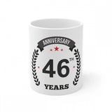White ceramic mug celebrating 46th anniversary with printed text and laurel wreath border