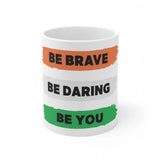 White ceramic mug with 'Be Brave Be Daring Be You' printed in multi-colored text and a rainbow stripe design