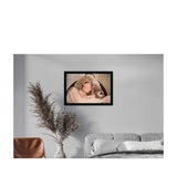 This is a framed, hand-painted canvas print of a baby in a blanket, set against a simple backdrop. The frame has a shiny, metallic finish and the painting is done with acrylic paint