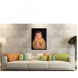 The image shows a multicolored baby photo painting with a rectangular frame displayed on a wall in front of a couch