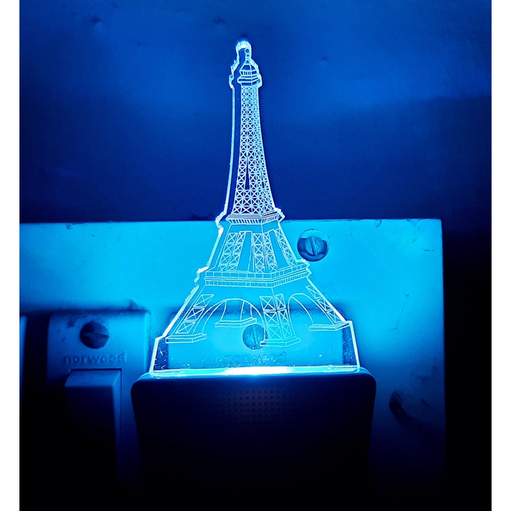 This is a photo of two images, the top one appears to be a night lamp with an Eiffel Tower design, featuring blue lighting. The bottom one shows a real-life object that resembles the same design but in the context of a plugged-in electronic device or appliance. It has a vibrant blue light and is designed with an Eiffel Tower motif on top