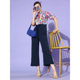 Women's navy blue 3/4 sleeve jumpsuit with a multicolored print, featuring high-waisted pants and a button-up front. The jumpsuit is paired with yellow strappy heels and a matching clutch purse