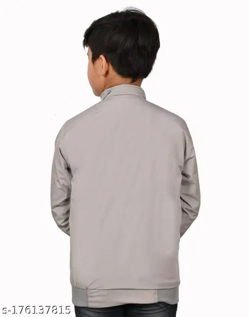 A young boy standing against a wall, wearing a grey sweater with zip closure