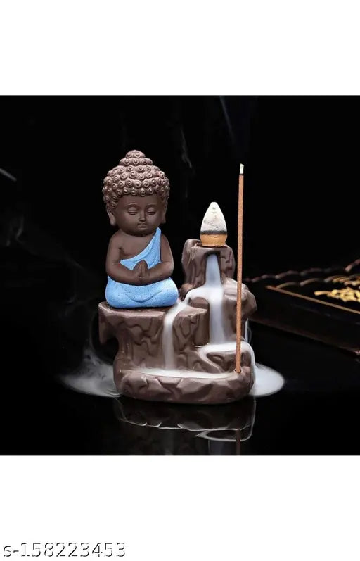 This is a decorative showpiece featuring a monk Buddha with a backflow cone incense holder. The statue of the Buddha appears to be crafted from a polished stone and has an intricate design, sitting on top of the incense holder. The holder is positioned in front of the Buddha, suggesting that it holds incense cones. There are no visible texts or branding on the statue or the incense holder