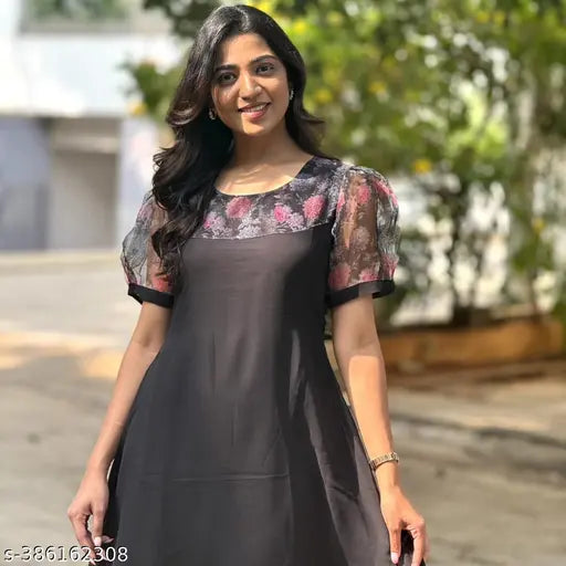 A woman posing in a dark kameez with lace detailing, set against a white wall