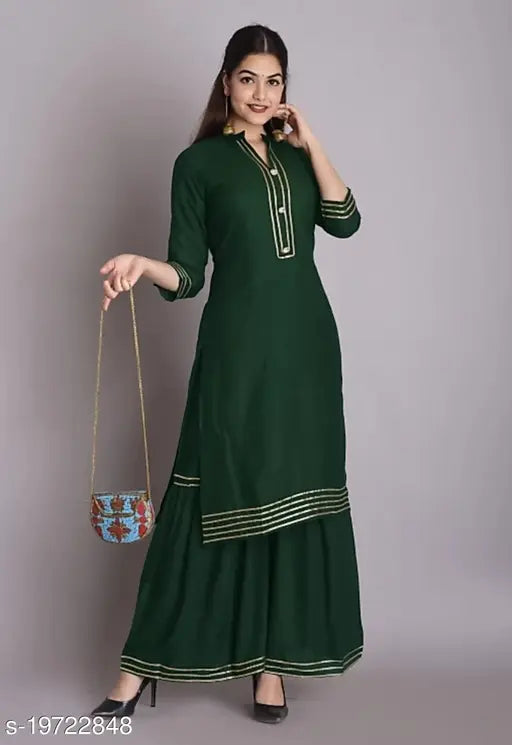 A woman wearing a dark green angiya straight kurta sharara set with gota lace, posing against a gray background