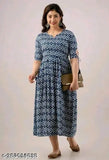 A woman wearing a long, blue, patterned dress. The dress has flared sleeves and appears to have a matching cardigan or jacket over it. She is carrying a small clutch purse and smiling at the camera