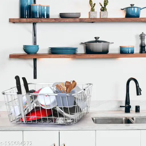 This is a steel dish drainer with one spoon holder. It sits on a counter, above which a shelf holds various kitchen items including bowls and a pot. The background features blue cabinets and a sink