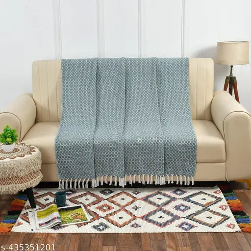 Cream couch with folded throw, patterned like a diamond weave, in shades of white, gray, and beige