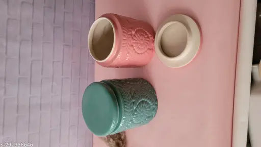 A green ceramic jar on a purple surface, next to a pink ceramic jar