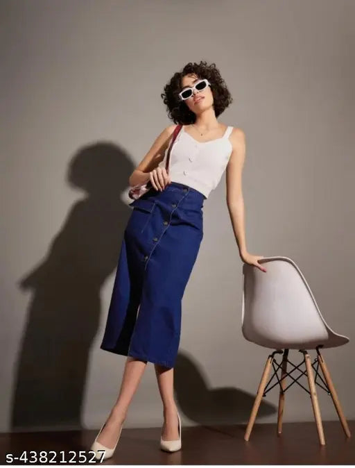 A woman in blue jeans and a white top stands against a gray wall. She wears sunglasses on her head, and there is a chair behind her