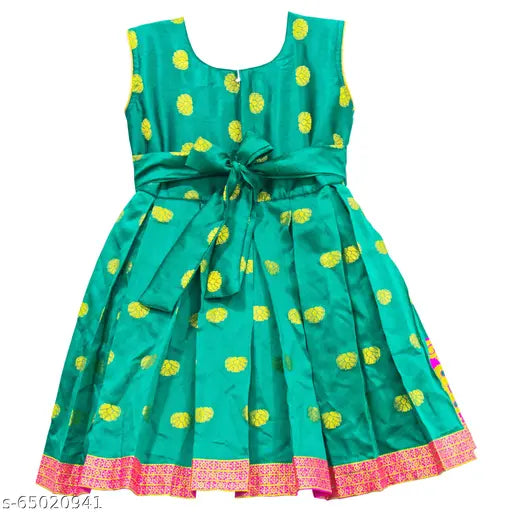 The image displays a vibrant green dress adorned with yellow polka dots, featuring an elastic waist accentuated by a large bow tie, and it is decorated with pink embroidery on the hem