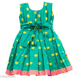 The image displays a vibrant green dress adorned with yellow polka dots, featuring an elastic waist accentuated by a large bow tie, and it is decorated with pink embroidery on the hem