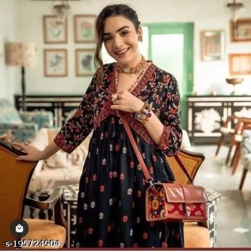 Woman wearing a blue floral dress with a black purse, posing in an indoor setting