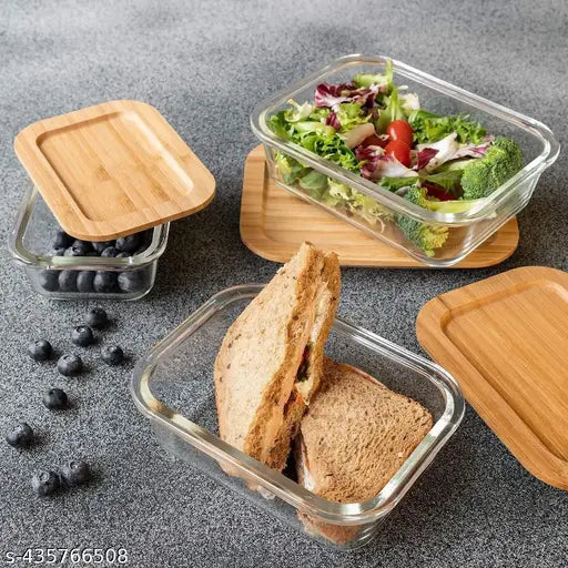 The image displays a set of modern clear jars with two stacked containers containing food. On top, there is a piece of bread. The jars are sealed and appear to have lids. One jar has a label that reads "Berry Blend." There is also a wooden board with blueberries nearby the jars. The text on the board is not legible in the image