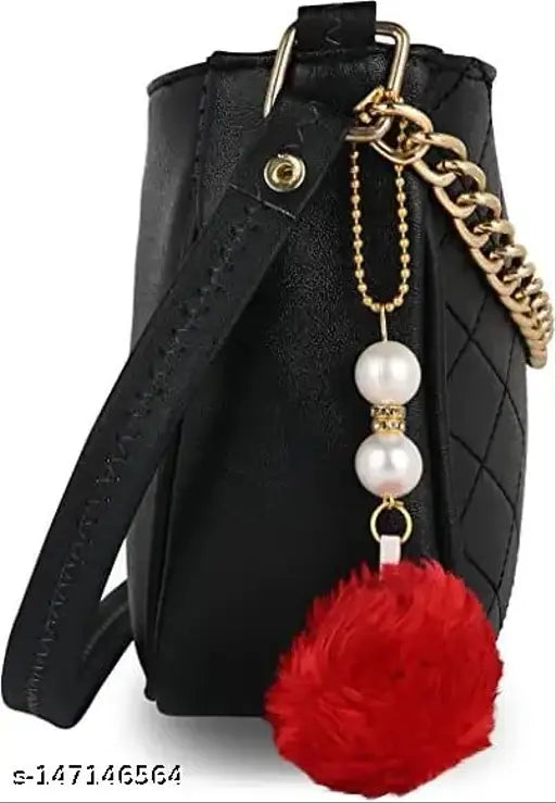 Black leather sling bag with a silver chain necklace and red pompom accent, featuring a zip closure