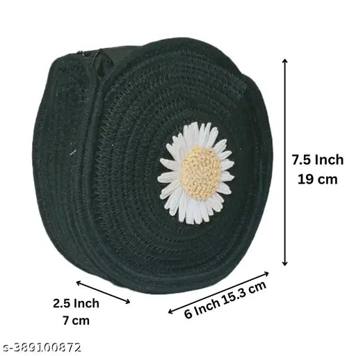 This is a black, jute and cotton sling bag with a flower adornment. It features a white flower embroidered on a black background and has a yellow center. The bag strap measures 75 cm in length