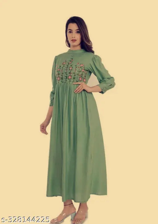 A woman wearing a long, green, enthic dress with a V-neckline and a fitted waist. The dress features nine ruffled bottoms and is made from reyon fabric. It has short sleeves and can be worn for various occasions like festivals or traditional events