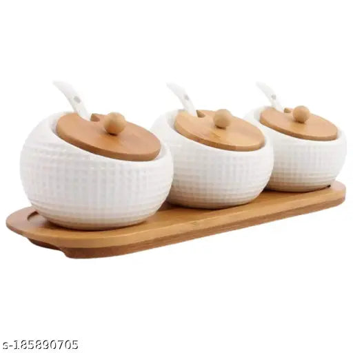 White ceramic jars in a set of three, each with a bamboo lid and a serving spoon in a wooden tray on a kitchen counter