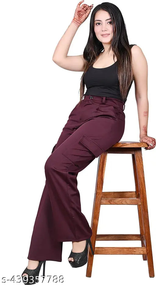 A woman poses against a plain background. She is wearing a maroon jumpsuit with a white top underneath, paired with black boots. Her hand is on her hip