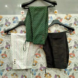 Green and blue fabric patterned pants, black waist belt, displayed on hanger against a floral background