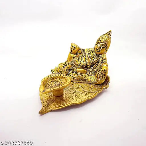 Gold metal figurine of Kuber, seated on a leaf, with an oil lamp at his feet. Deepak style lamp with intricate detailing