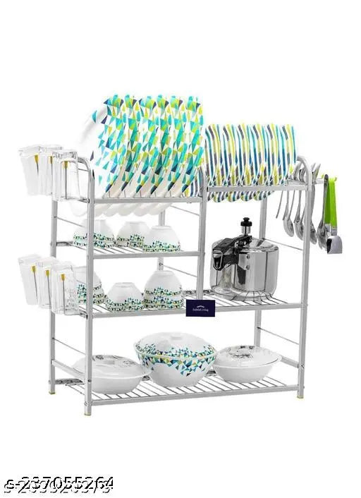 Stainless steel wall-mounted kitchen utensils rack with four shelves and a plate holder on top, containing various spoons, glasses, and bowls
