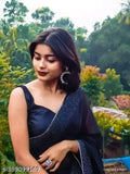 Woman in black sari, dark eye makeup, standing outdoors