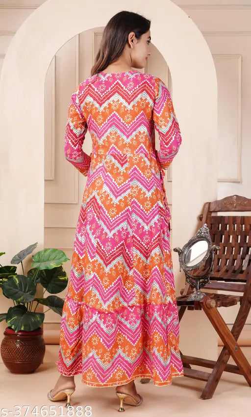 The image displays a long, full-length kurta with heavy gold foil print and embroidery. It is worn by a person standing next to an indoor setting with furniture