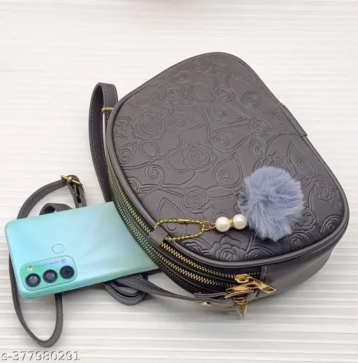 Black faux leather slingbag with pompom trim, multiple card slots, detachable camera strap