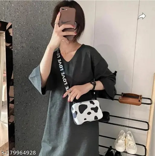 A person taking a selfie with a phone, wearing a long-sleeved black dress and holding a cow print clutch