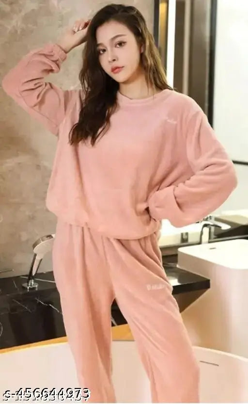 A woman in a pink sweat suit, standing against a beige backdrop, with her left hand resting on her hip
