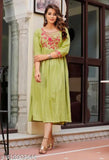 A person in a green kameez dress with embroidery, standing by a door