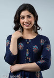 A woman in a navy blue sleeveless blouse with embroidered borders and black pants, posing with one hand on her hip