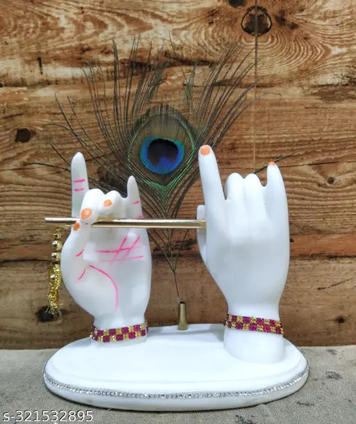 A hand, painted in blue hues, holding a pink bansuri while the other hand is raised to form a peace sign with pink nail polish. The hand is on a white statue of Lord Krishna, positioned against a wooden wall