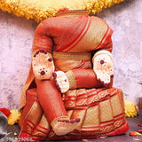 Red and gold traditional saree fabric adorned with a seated varalakshmi idol, embellished with flowers