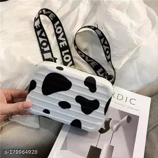 A black and white cow patterned sling bag with a zip closure