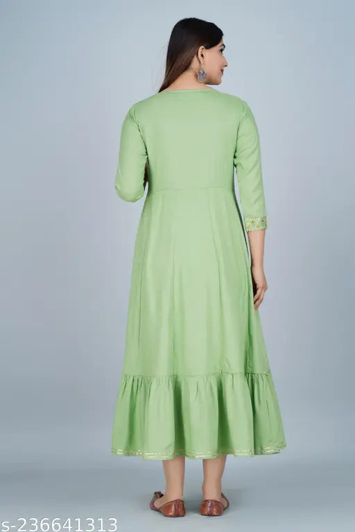 A woman wearing a light green anarkali kurta with embroidery details, possibly satin fabric, long sleeves, and a traditional ruffled hem