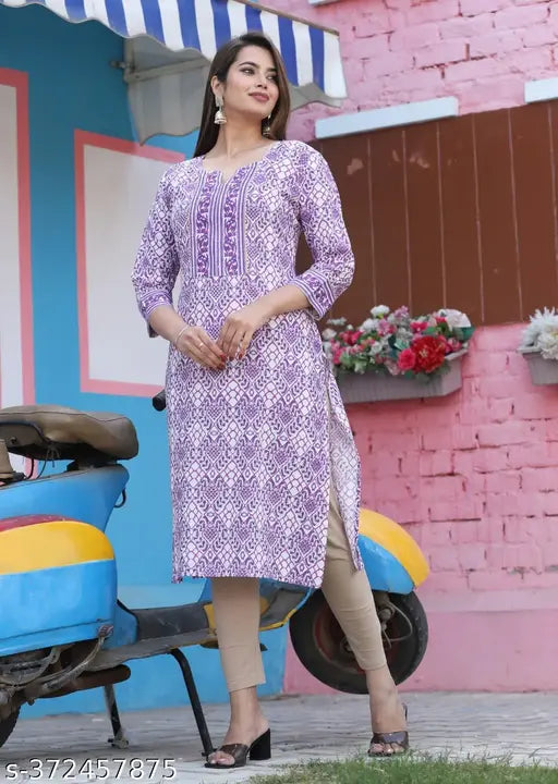 A woman wearing a purple and blue patterned kurta standing in front of a pink building