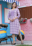 A woman wearing a purple and blue patterned kurta standing in front of a pink building