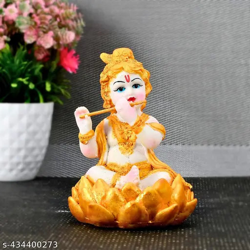 Golden metal statue of Krishna as a baby, poised in a seated pose with lotus leaf in hand and flanked by two hands on knees, all within lotus flower motif base. Home decor piece