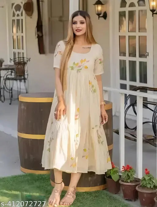 Woman in long, flowing beige kameez with floral design, standing outside with wine barrel in background