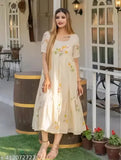 Woman in long, flowing beige kameez with floral design, standing outside with wine barrel in background