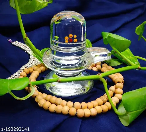 Transparent crystal figure representing Shiva lingam, set against a blue background with leaves, resting on a bed of beads