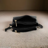 Black leather sling bag with adjustable strap, large front zip pocket, and small side pockets